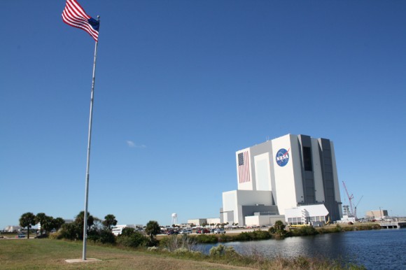 My view of the Vehicle Assembly Building (VAB) adjacent to the Kennedy Space Center Press Center. Shuttles are prepped for flight inside the rectangular box shaped buildings at left (near water tower) known as the Orbiter Processing Facility (OPF). At right see the Launch Control Center (LCC). Ares 1 rocket gantry under construction with tall crane to right of VAB. Credit: Ken Kremer