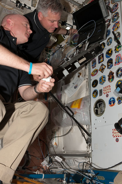 Commander Mark Kelly and Greg Johnson looks at the various mission insignias placed in the Unity node of the International Space Station before placing the STS-134 insignia among them. Credit: NASA