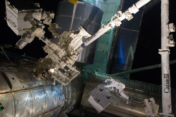 With his feet secured on a restraint on Canadarm2, Mike Fossum holds the Robotics Refueling Mission payload. The failed pump module is with DEXTRE in the upper left corner of the photo. The blue color on the space station module is a reflection from the blue of planet Earth. Credit: NASA