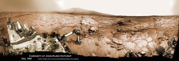 Curiosity accomplished Historic 1st drilling into Martian rock at John Klein outcrop on Feb 8, 2013 (Sol 182), shown in this context mosaic view of the Yellowknife Bay basin taken on Jan. 26 (Sol 169). The robotic arm is pressing down on the surface at John Klein outcrop of veined hydrated minerals - dramatically back dropped with her ultimate destination; Mount Sharp. Credit: NASA/JPL-Caltech/Ken Kremer/Marco Di Lorenzo