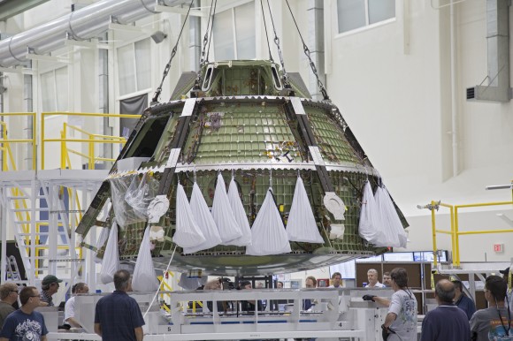A crane lifts the Orion EFT-1 crew module from its birdcage processing stand for transfer it to a dolly for continued assembly inside the Operations and Checkout Building high bay at NASA’s Kennedy Space Center in Florida as workers monitor progress. Orion’s first unpiloted test flight is scheduled to launch in 2014. Credit: NASA/Frankie Martin