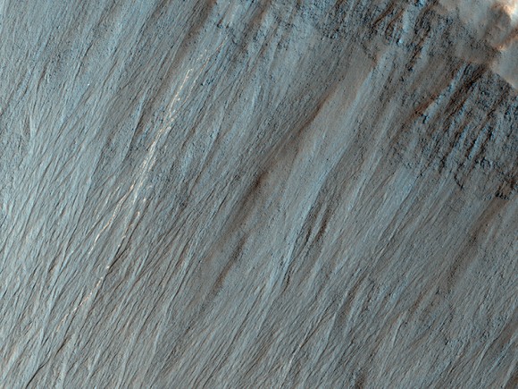A closeup of an impact crater shows distinctive bright lines and spots on the steep slope, indicating bouncing boulders have fallen down the incline. Credit: NASA/JPL/University of Arizona. 