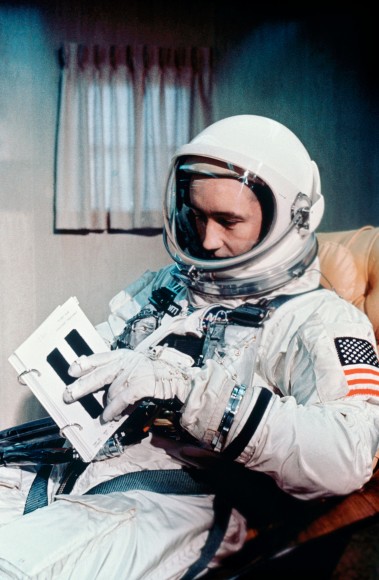 Gemini 4 astronaut Jim McDivitt reviewing a crew procedures book in a trailer on the way to the launch pad. His flag was on the left shoulder. Credit: NASA