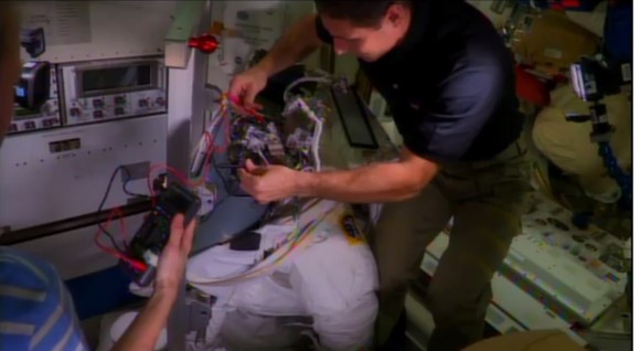 NASA astronauts Mike Hopkins and Karen Nyberg (edge of picture, at left) examine a faulty spacesuit aboard the International Space Station during Expedition 37 in October 2013. In July 2013, Italian astronaut Luca Parmitano had to abort a spacewalk after a water leak arose while wearing the spacesuit. The cause is still under investigation. Credit: NASA/YouTube (screenshot)