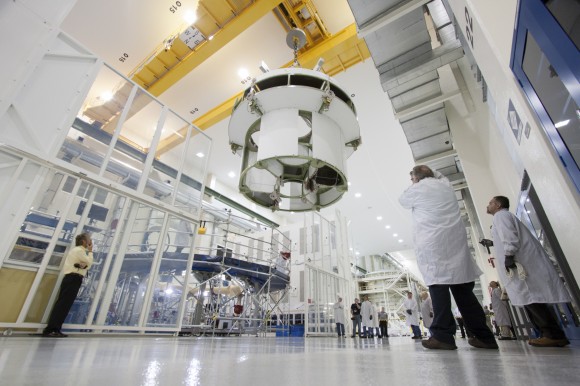 Inside the Operations and Checkout Building high bay at NASA’s Kennedy Space Center in Florida, a crane moves the service module for the Orion spacecraft toward a lift station where it will be mated to the spacecraft adapter cone. Photo credit: NASA/Jim Grossmann