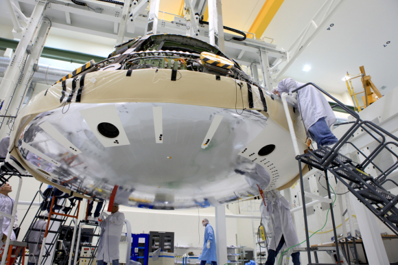 Orion heat shield attached to the bottom of the capsule by engineers during assembly work inside the Operations and Checkout High Bay facility at KSC. Credit: NASA