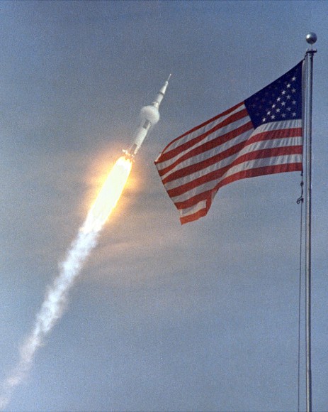 Apollo 11 Launch. The American flag heralded the launch of Apollo 11, the first Lunar landing mission, on July 16, 1969. The massive Saturn V rocket lifted off from NASA's Kennedy Space Center with astronauts Neil A. Armstrong, Michael Collins, and Edwin "Buzz" Aldrin at 9:32 a.m. EDT. Four days later, on July 20, Armstrong and Aldrin landed on the Moon's surface while Collins orbited overhead in the Command Module. Armstrong and Aldrin gathered samples of lunar material and deployed scientific experiments that transmitted data about the lunar environment. Credit: NASA