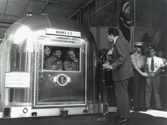 President Nixon Greets the Returning Apollo 11 Astronauts. The Apollo 11 astronauts, left to right, Commander Neil A. Armstrong, Command Module Pilot Michael Collins and Lunar Module Pilot Edwin E. "Buzz" Aldrin Jr., inside the Mobile Quarantine Facility aboard the USS Hornet, listen to President Richard M. Nixon on July 24, 1969 as he welcomes them back to Earth and congratulates them on the successful mission. The astronauts had splashed down in the Pacific Ocean at 12:50 p.m. EDT about 900 miles southwest of Hawaii. Credit: NASA