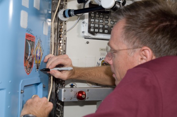 NASA astronaut Chris Ferguson, who commanded STS-135, signs a decal for his mission (the last space shuttle mission) in the Quest airlock of the International Space Station. Next to it is the crew patch for Expedition 28. Credit: NASA