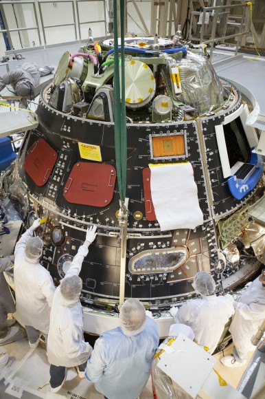 Inside the Operations and Checkout Building high bay at NASA's Kennedy Space Center in Florida, technicians dressed in clean-room suits have installed a back shell tile panel onto the Orion crew module and are checking the fit next to the middle back shell tile panel. Preparations are underway for Exploration Flight Test-1, or EFT-1. Credit: NASA/Dimitri Gerondidakis